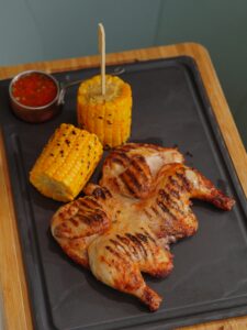 Delicious grilled chicken with roasted corn and spicy sauce on a tray.