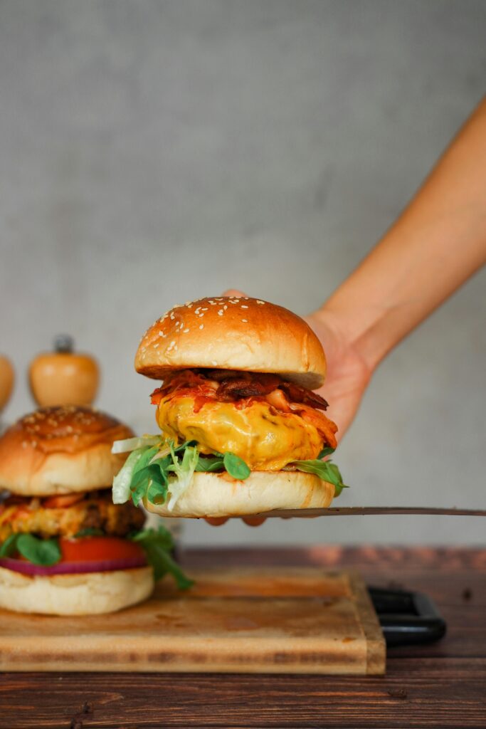 Close-up of a juicy cheeseburger with fresh toppings on a spatula, showcasing delicious food photography.