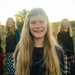 Outdoor group portrait of smiling teenage girl with friends in a field during sunset.
